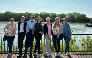 Foto zeigt Teammitglieder der PULSAR Medical AG, die das 3-jährige Jubiläum von PULSAR Medical AG feiern. Die Teammitglieder stehen in einer Reihe vor einem Zaun, dahinter ist ein See zu sehen mit einem Schiff. Die Sonne scheint und alle Teammitglieder sind am lächeln.