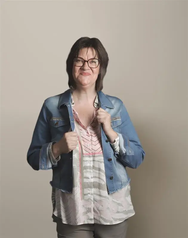 Woman wearing a denim jacket and glasses, smiling while holding the jacket's collar.