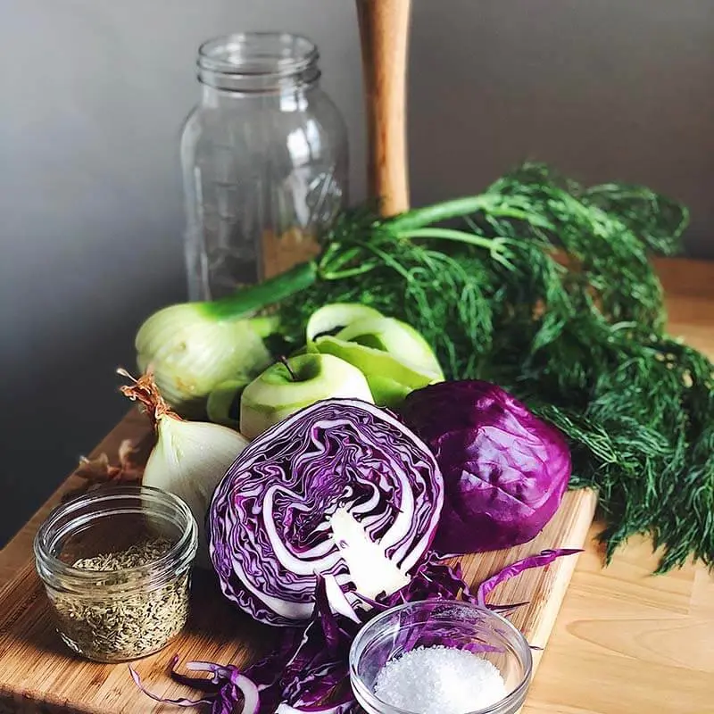 Frisches Gemüse und Gewürze auf einem Holzbrett, darunter Rotkohl, Zwiebeln und Dill.
