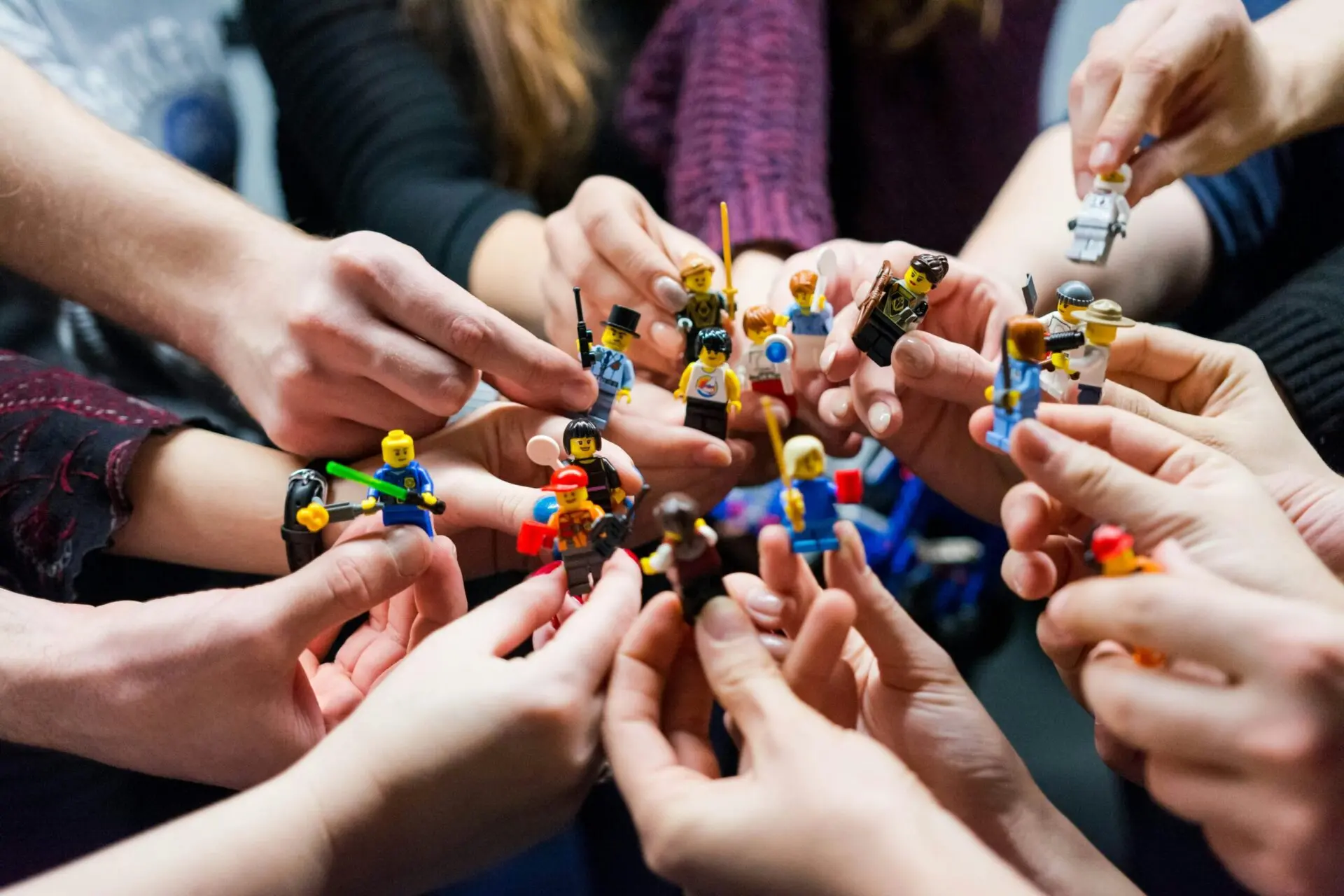 Mehrere Hände halten verschiedene LEGO-Figuren in einem Gruppenbild.
